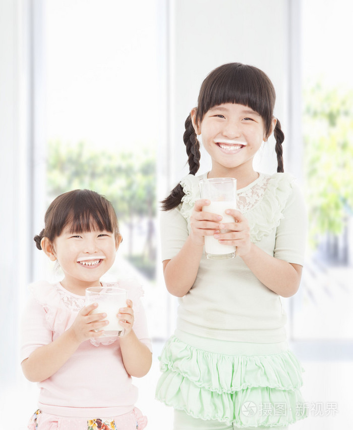 两个小女孩拿一杯新鲜的牛奶
