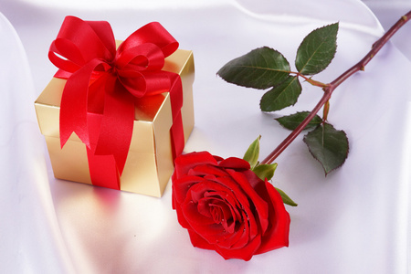 黄金礼品包装盒和红色玫瑰白色缎背景上