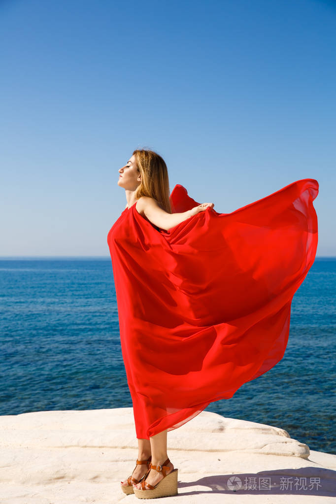 在塞浦路斯海滩的红色礼服漂亮的金发女郎