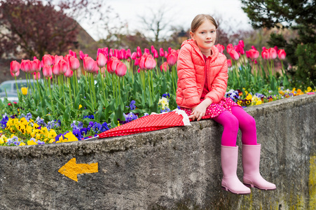 女雨靴可爱的小女孩,坐在旁边花坛充分的郁金香,穿着亮粉色的衣服和