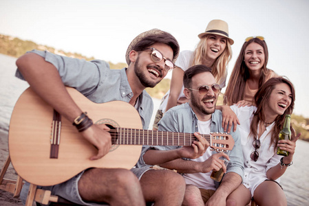 一群快乐的年轻人在沙滩上野餐, 玩吉他, 一起玩得开心。