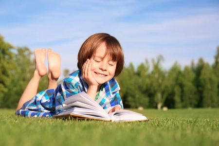可爱的小男孩在公园读书在晴朗的天