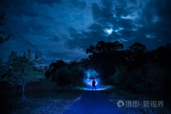 晚上在森林里的人的剪影.人的剪影站在黑暗的森林与光.森林里的黑夜.