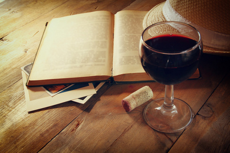 红葡萄酒杯和老本打开的书在日落爆裂木制的桌子上。老式的滤波的图像