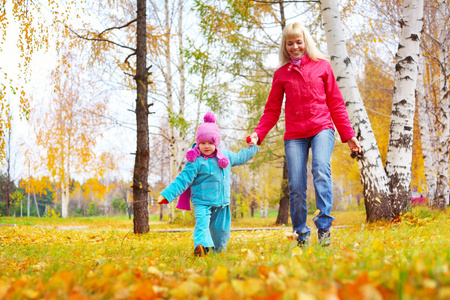 快乐年轻的母亲和她的小女儿走在秋天的公园