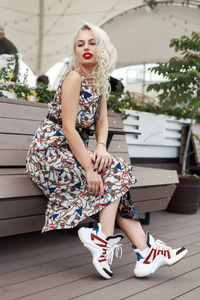 美丽的年轻时尚的女孩在老式时装礼服与模式坐在一个木凳在城市