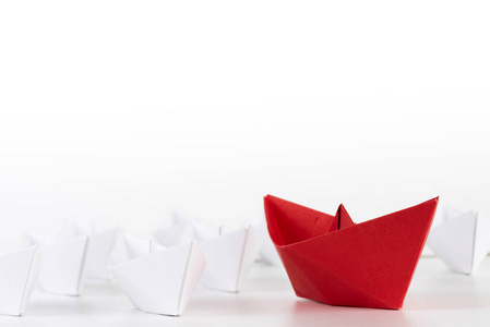 领导理念。红纸船在白色中领先。一个领导船带领其他船