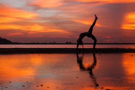 年轻女人上练瑜伽的湖在日落时的剪影