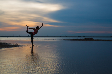 年轻女人上练瑜伽的湖在日落时的剪影