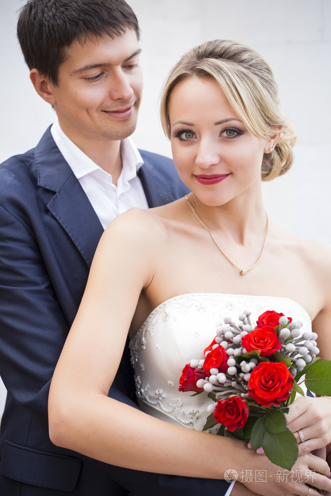 接吻的结婚礼服的年轻夫妇新娘紧握着红玫瑰花束