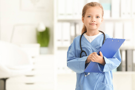 可爱的小女孩在医生制服与剪贴板在医院