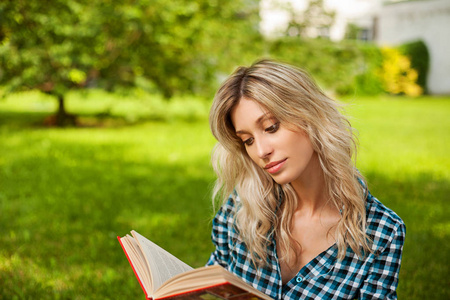 年轻的金发女子阅读书, 而坐在公园