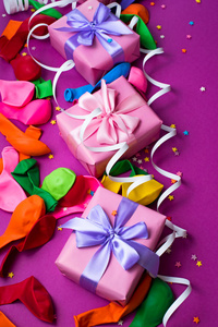 节日背景的紫色材料五颜六色的气球彩带五彩纸屑盒礼物。顶部视图平躺复制空间