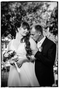 新婚夫妇在绿色的夏天公园接吻。新郎和新娘接吻，在户外站在一起，拥抱在绿树之间。新娘抱着婚礼花束