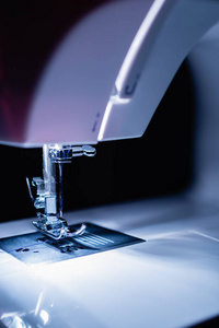 现代紧凑型电动缝纫机在傍晚。针和螺纹的看法。内置白炽灯照明。缝纫机是用来缝合织物和其他材料一起