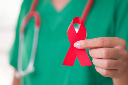 女医生用听诊器在肩上抱着红丝带 Hiv, 世界艾滋病日意识丝带。医疗保健和医学概念