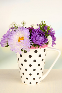 束美丽的鲜艳的花朵颜色杯里木桌上，轻的背景上