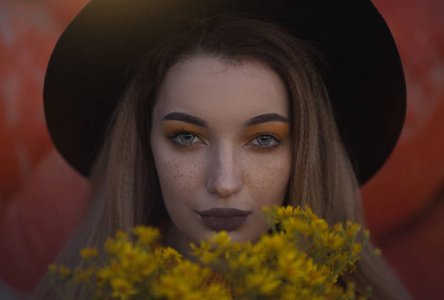 一个戴着帽子和黄色花朵的女孩的舒适的秋天照片肖像