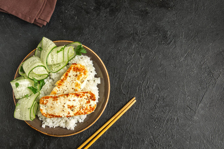 豆腐牛排配米饭和黄瓜沙拉, 黑色背景, 复印空间。健康素食素食餐配烤炸豆腐牛排