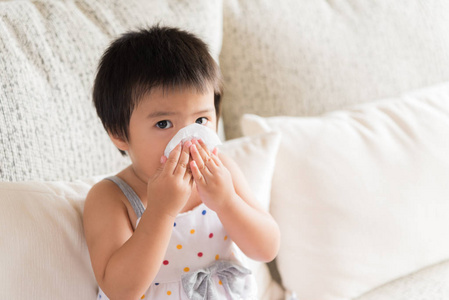 生病的小亚洲女孩擦或清洁鼻子与组织坐在沙发上的家。医疗保健理念