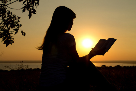 一个女孩在日落时阅读的剪影