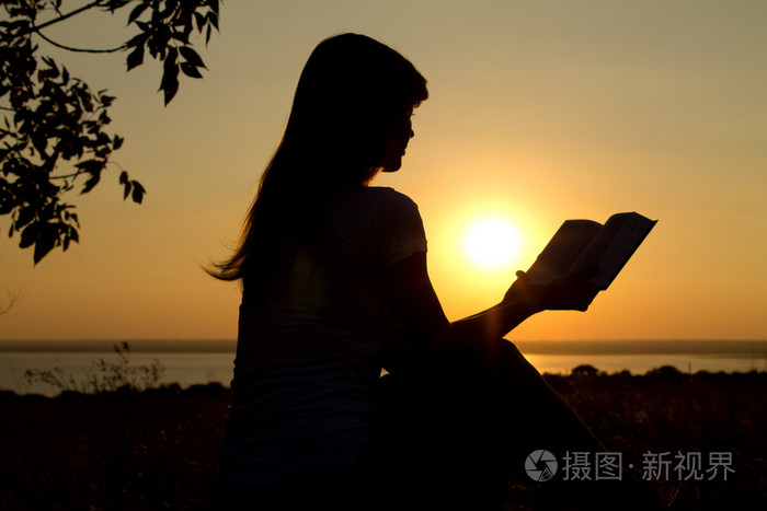 一个女孩在日落时阅读的剪影