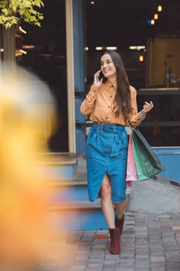 年轻时尚的女人与购物袋谈论智能手机在城市街