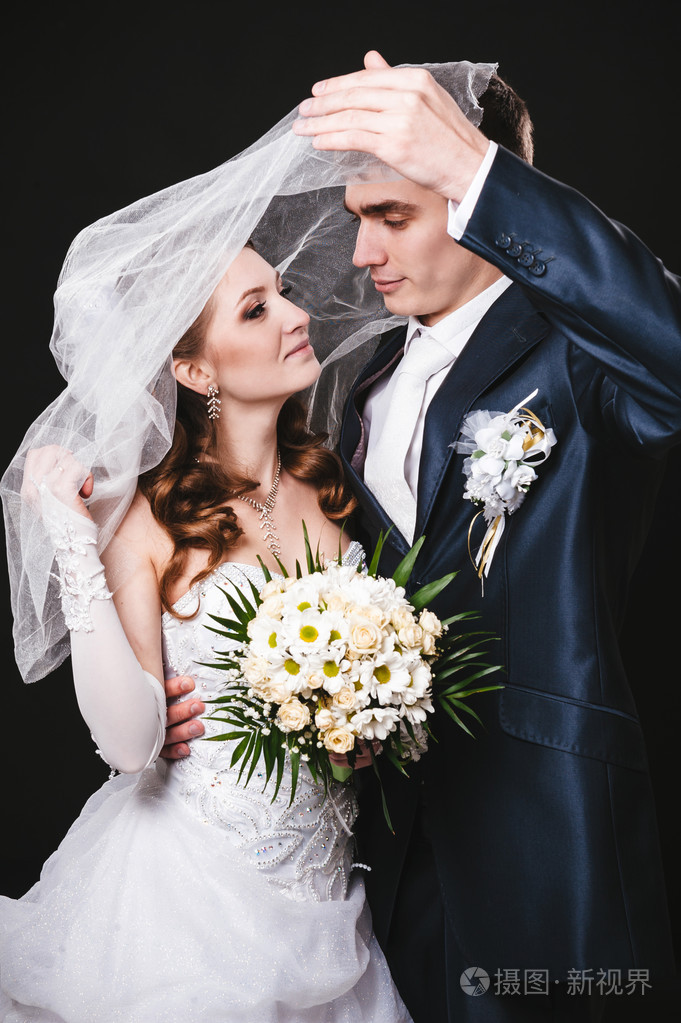 照片 新娘和新郎亲吻下手持鲜花花束的面纱.黑色背景.