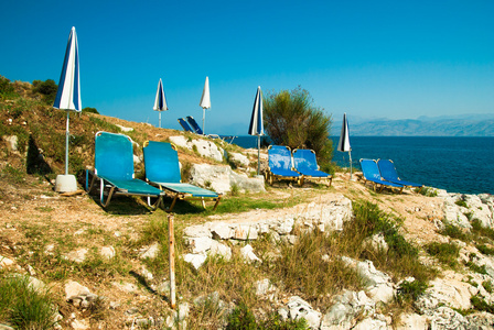 日光浴浴床和伞 阳伞 在科孚岛 Islan 的岩石海滩上