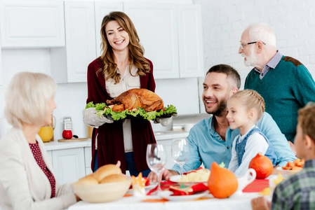 美丽的微笑的妇女携带烤火鸡与家庭感恩节晚餐