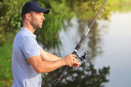 钓鱼。渔夫在河与钓鱼竿。日落时分在湖边钓鱼。狩猎和爱好