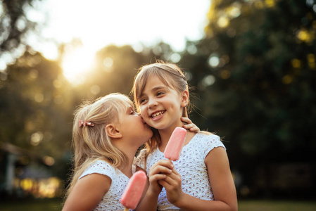 两个年轻姑娘耳语时在日落时在户外吃冰激淋