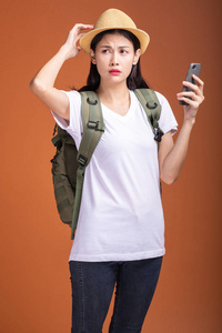 年轻的时髦游客使用手机。亚洲女人带着背包, 帽子在寻找帮助。混淆情绪。时髦的度假概念