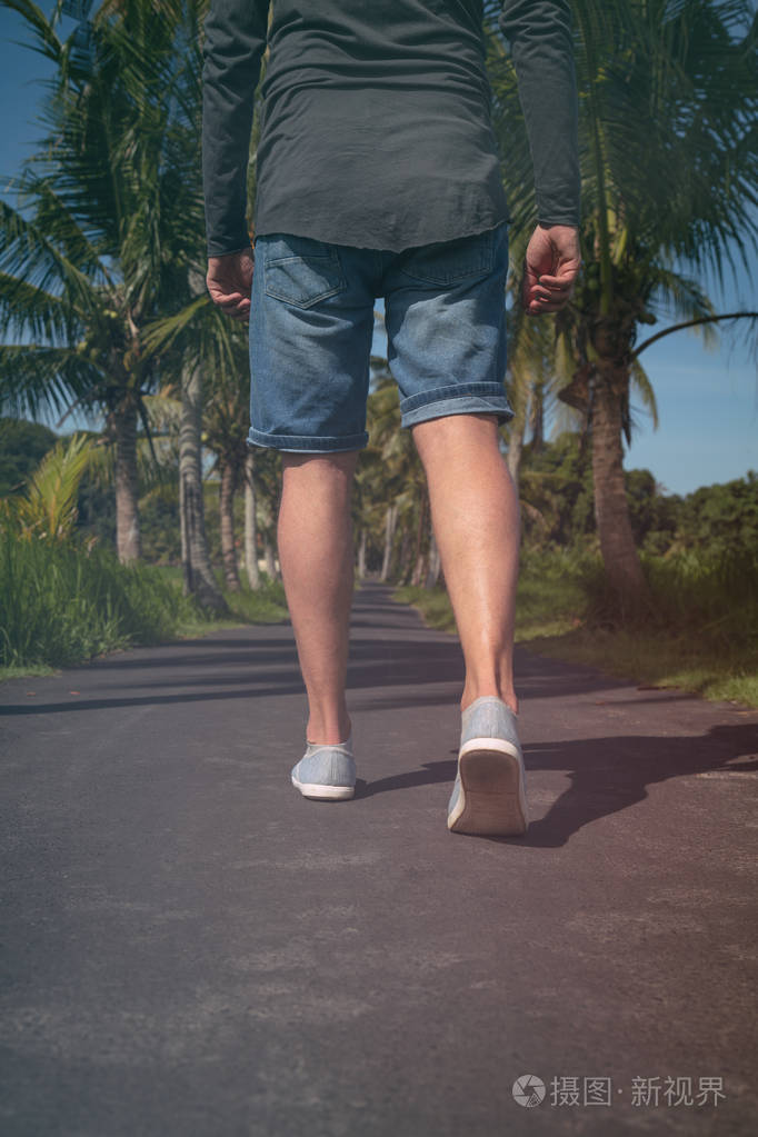 一个男人的背部的细节而步行通过与棕榈树的街道