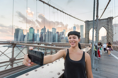 年轻漂亮的女人在布鲁克林大桥上采取拍照