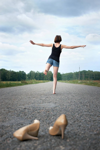 年轻的女孩赤脚走在路上, 她把鞋子丢在路上忘了他们, 夏天和旅行的概念