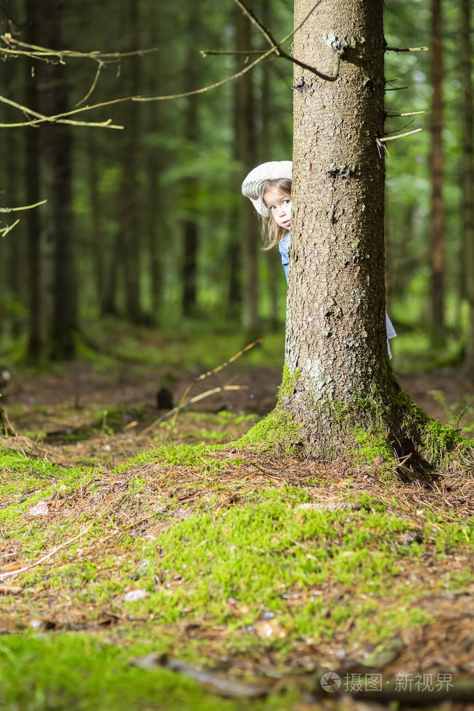 在绿色夏日森林里潜伏在树上的高加索小女孩的画像.垂直图像