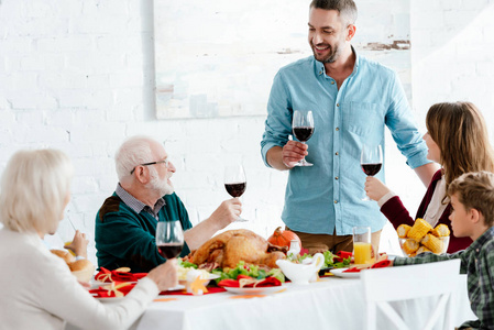 成年男子与葡萄酒玻璃做土司, 而他的家人在感恩节假期晚餐