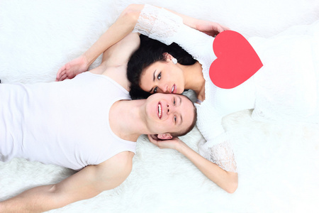 年轻可爱的情侣举行红色的心在一起躺在床上的情人节