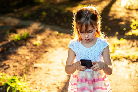 年轻的小女孩在公园里使用移动电话的肖像