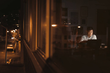 年轻的亚洲商人在办公桌前深夜工作在办公大楼窗户后面反映城市
