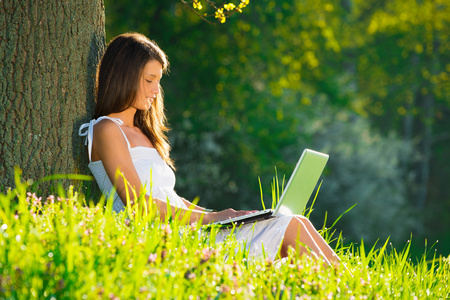 美丽的年轻女子与笔记本电脑的草地上放松