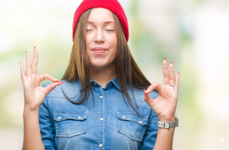 年轻的高加索美丽的女人穿着羊毛帽在孤立的背景放松和微笑闭着眼睛做冥想手势用手指。瑜伽概念