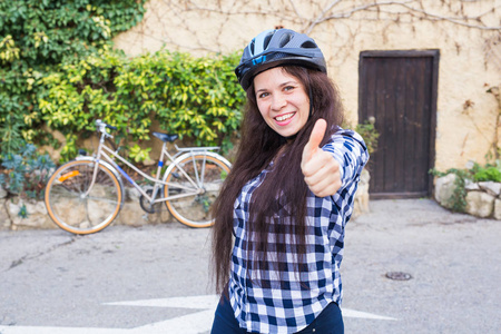 戴头盔和太阳镜的年轻女子在背景小巷和自行车上显示拇指上