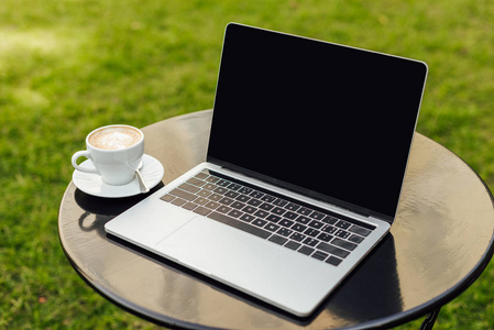 带空白屏幕和咖啡杯的笔记本电脑在花园里的桌子上