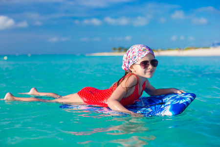可爱的小女孩在一个冲浪板在绿松石海中游泳