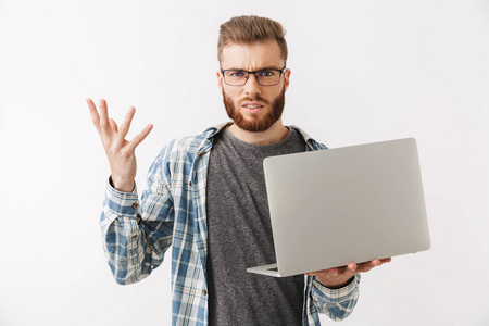 不满胡子的人在衬衫和眼镜持有笔记本电脑, 而看着在灰色背景相机