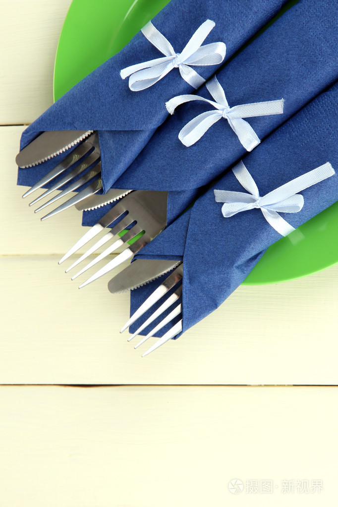 包裹在蓝色纸餐巾彩色木制背景上的刀子和叉子