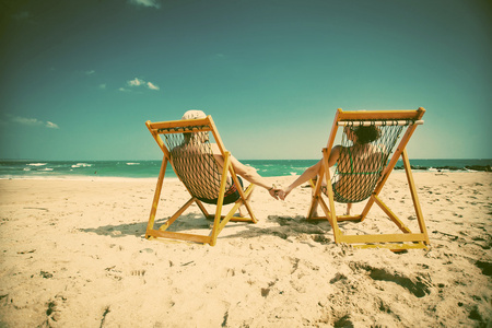 对情侣坐在沙滩椅和手牵着手在热带 b