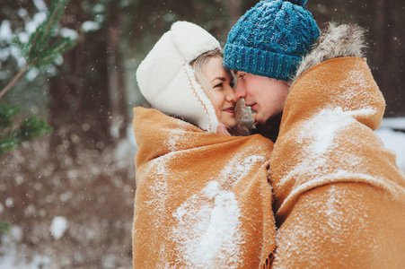 快乐的年轻情侣漫步在白雪皑皑的冬季森林, 覆盖着特大的围巾和拥抱。户外活动冬季假期